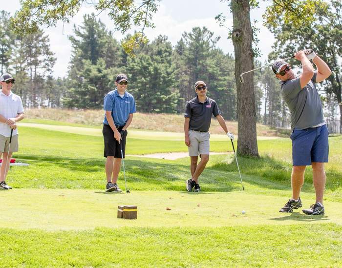 Golfer driving off the tee as his group watches