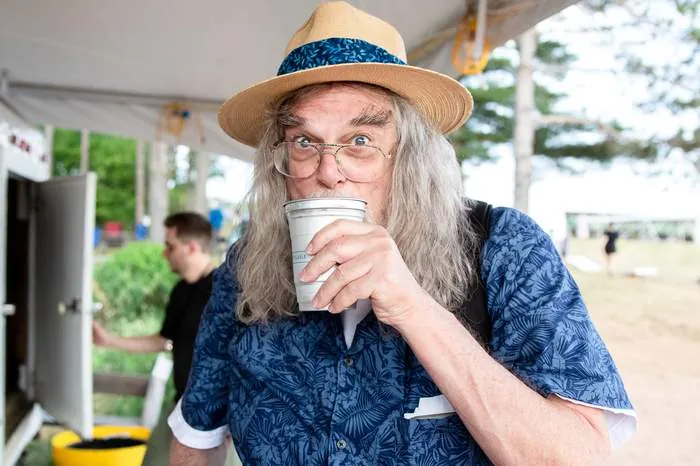 Guest sipping a drink under the festival tent, straw hat and Hawaiian shirt