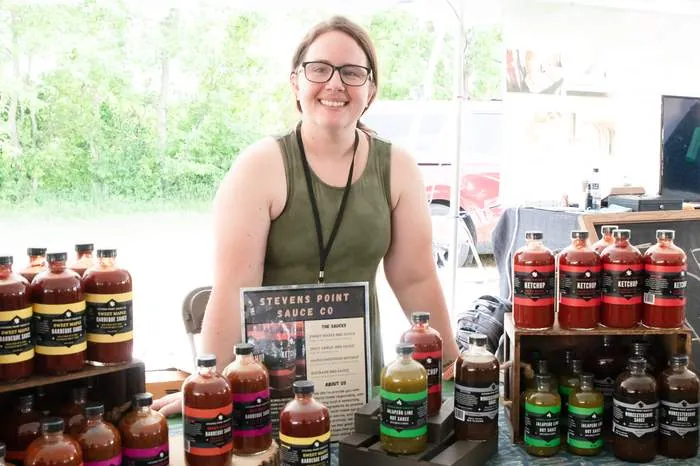 Vendor smiling behind her table of bottled sauces at a community fair