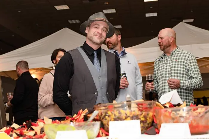 Guest in vest and tie smiling at a reception, appetizer table in foreground