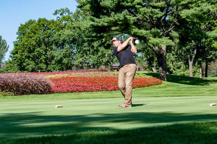 Golfer teeing off beside a flower bed at a charity golf outing