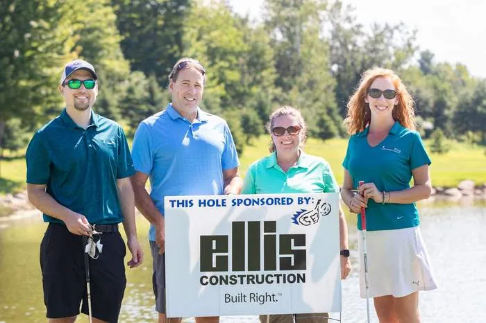 Golf outing group posing at a sponsor tee sign