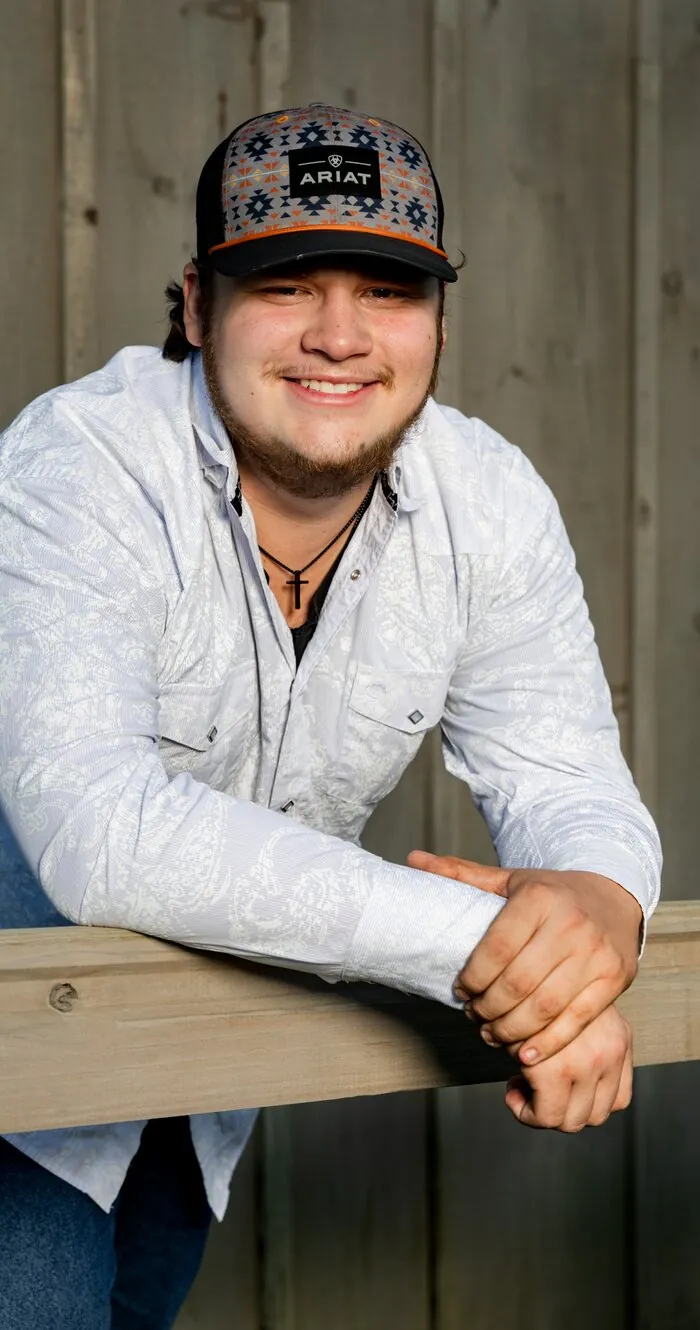 Senior portrait leaning on a fence rail, warm smile
