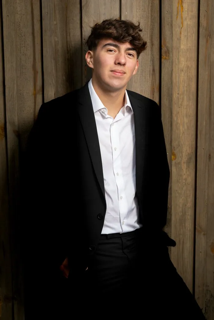 Senior portrait in a suit against a rustic wood wall