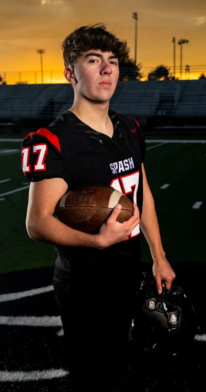 Senior football portrait on the field at sunset, holding helmet and ball